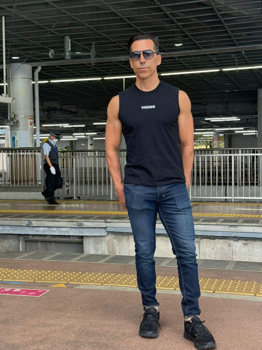Man wearing black Viking Tank Top with jeans and sunglasses at train station platform