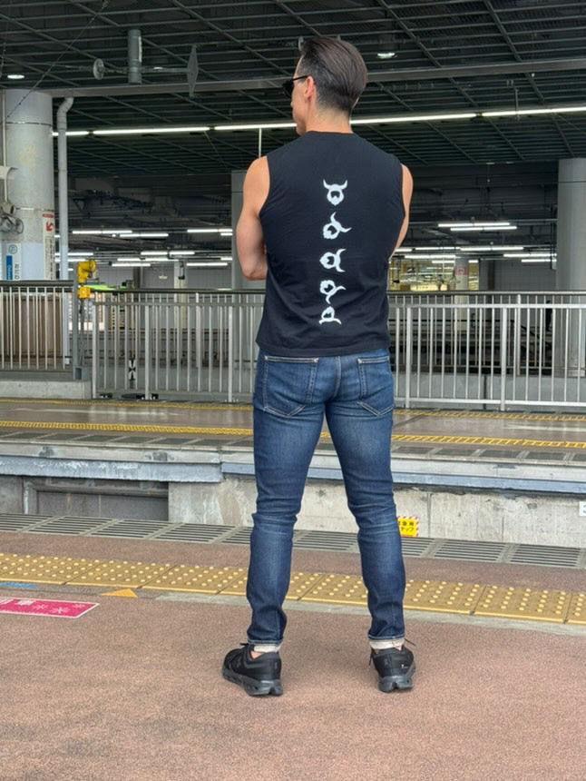Man wearing black Viking Tank Top with white Viking runes design on back, paired with jeans at outdoor train station