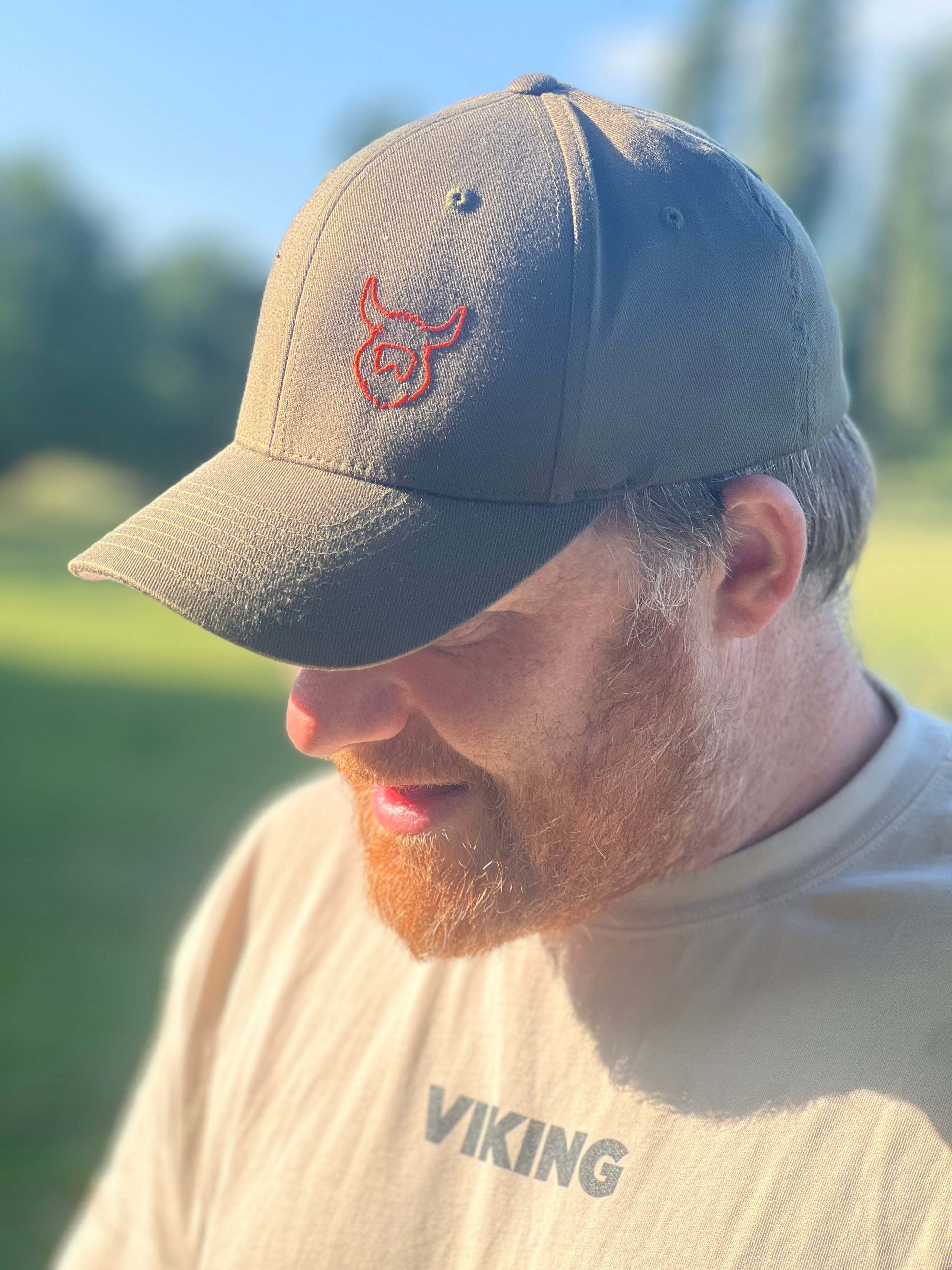 Man wearing olive green Flexfit Viking Hat with red embroidered Viking logo outdoors