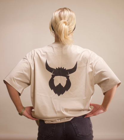 Back view of apricot Viking t-shirt with black Viking helmet and beard logo on the back, worn by a person with blonde hair tied in a ponytail.