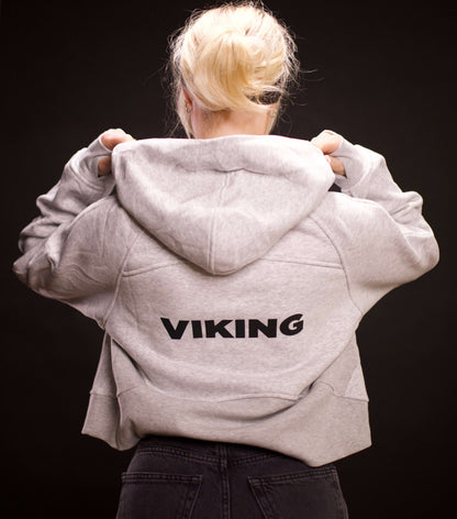 woman wearing light gray cropped Viking hoodie with hood up showing black Viking text on back against dark background